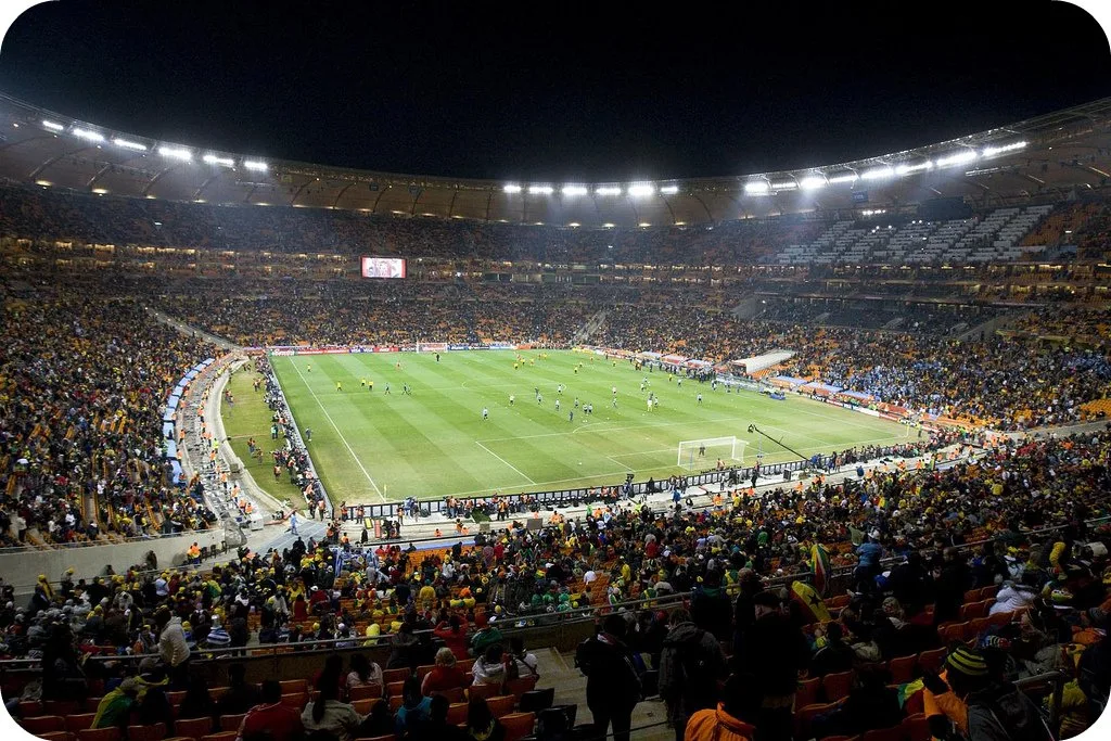 A packed football stadium crowd under floodlights on match night.