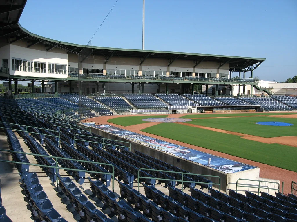 Rows of empty seating overlook a baseball diamond at a stadium.